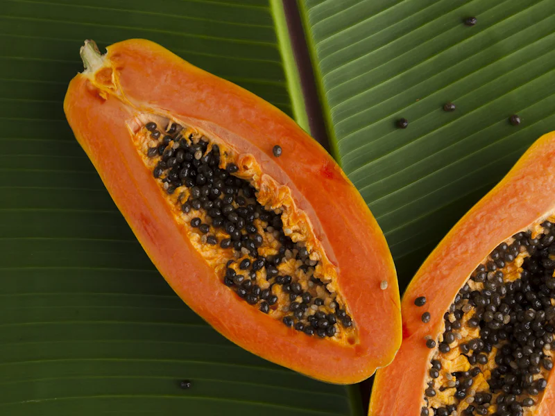 Halved papayas resting on a green banana leaf.